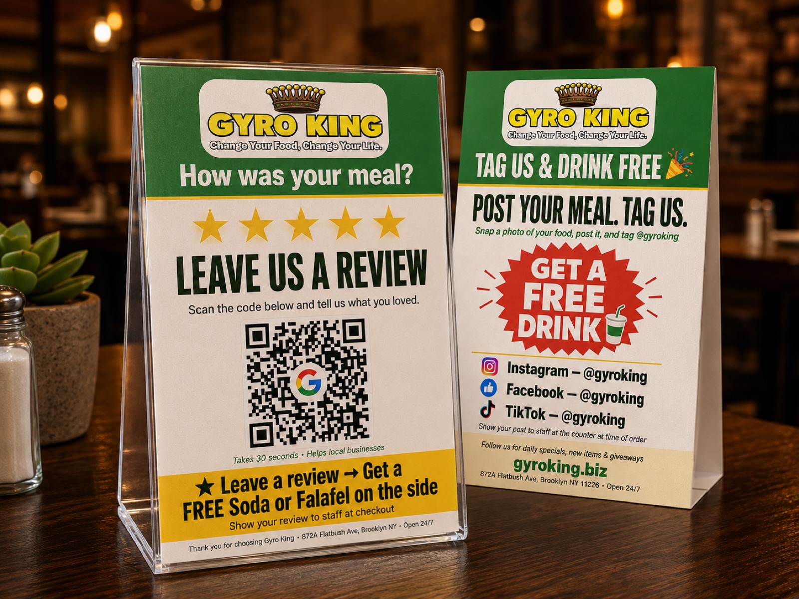 Two printed Gyro King table tents on a restaurant table: one with five gold stars, the words Leave Us a Review and a QR code to the Google review form, the other inviting diners to post their meal and tag the restaurant on Instagram, Facebook and TikTok